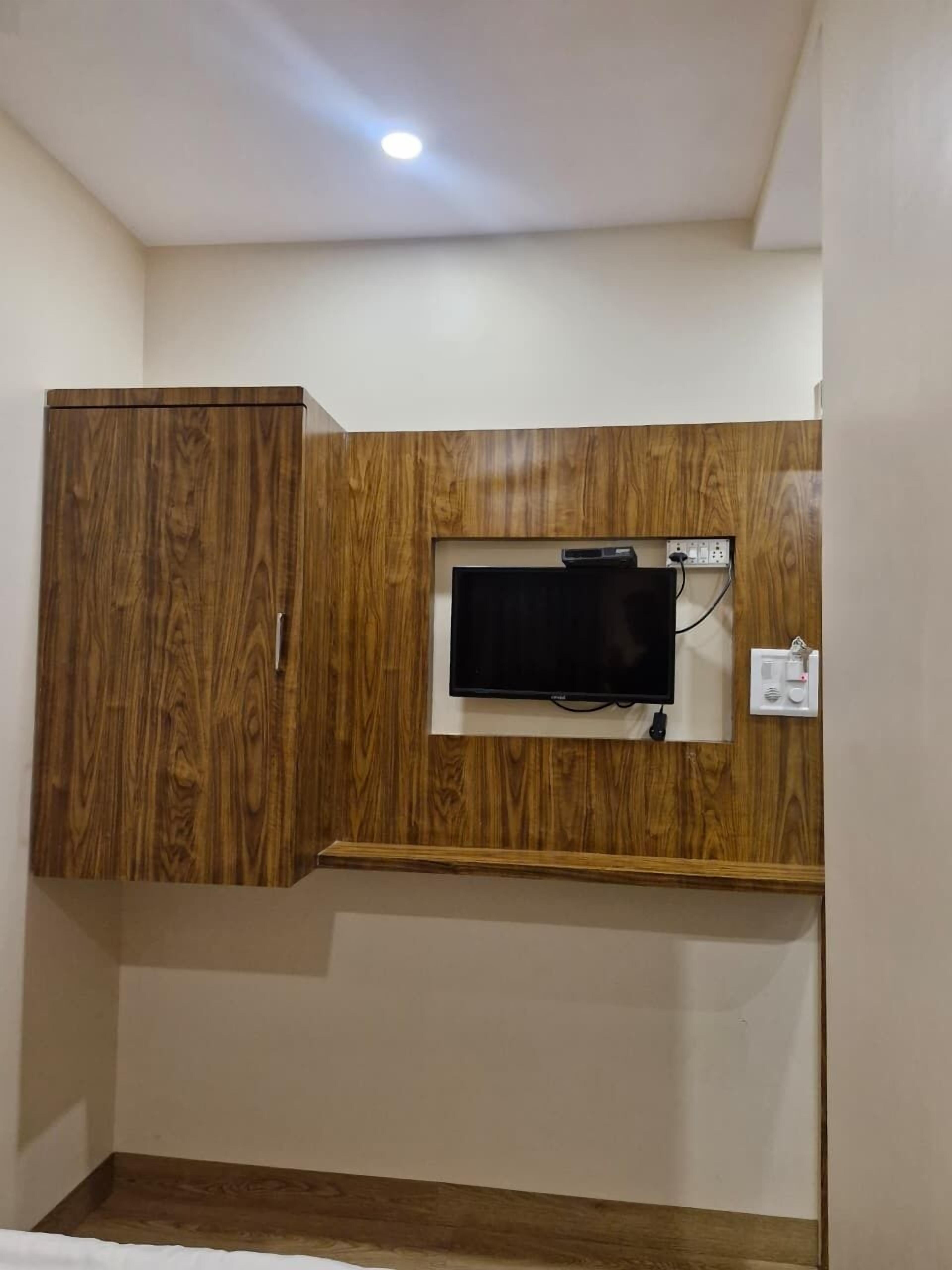 A room with a wooden wardrobe, a mounted television, and a power outlet on the wall.