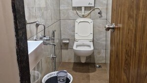 A compact bathroom with a toilet, bidet, and sink. A bucket with a lid is placed on the floor. - Hotel AL-HAMD (Mumbai)
