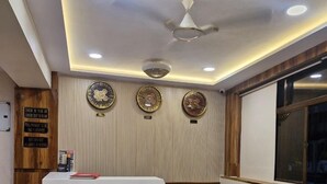 A reception area with a wooden reception desk, a ceiling fan, and three wall clocks. - Hotel AL-HAMD (Mumbai)