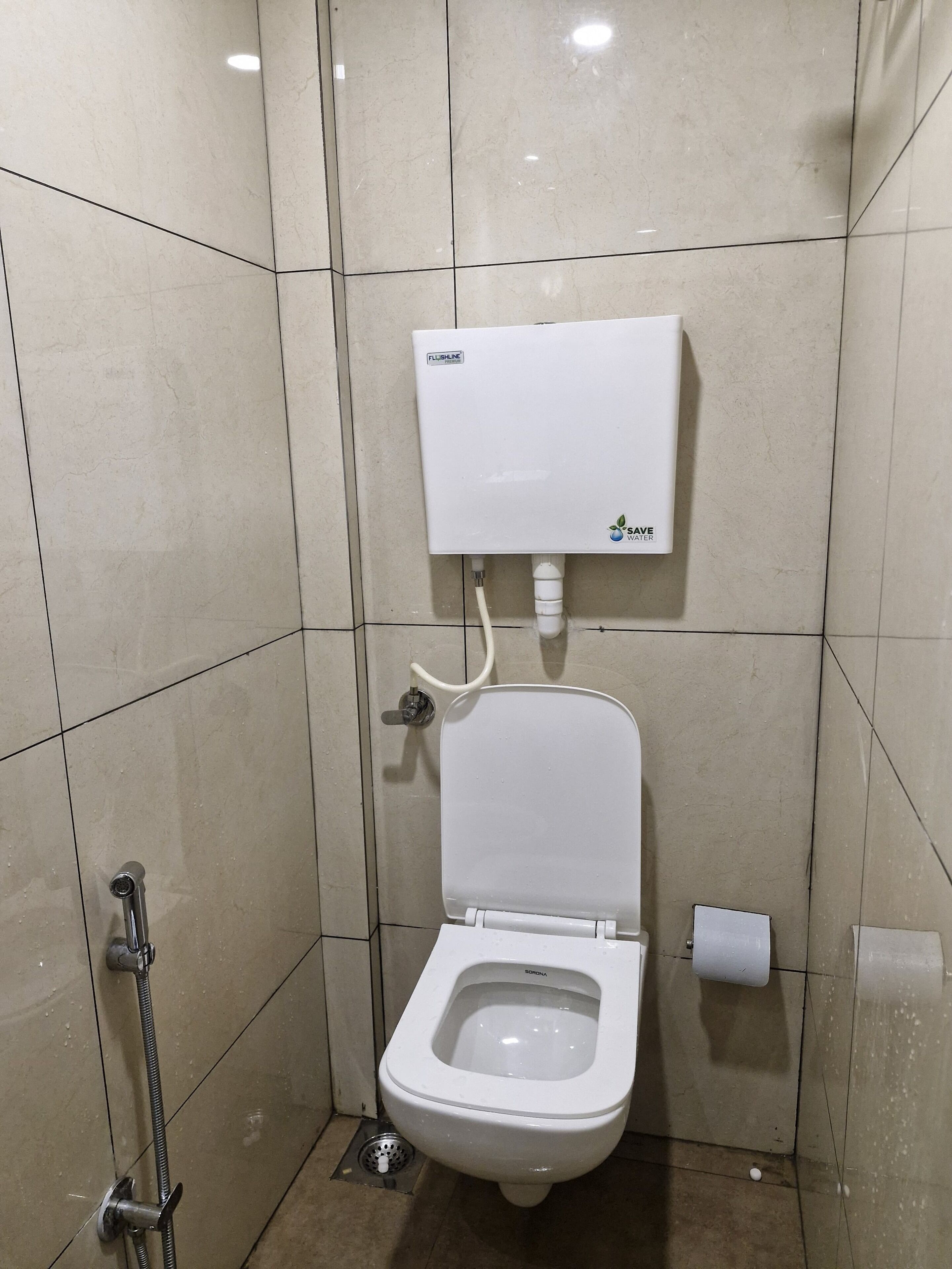 A small, tiled bathroom with a toilet, a flush tank, and a showerhead.
