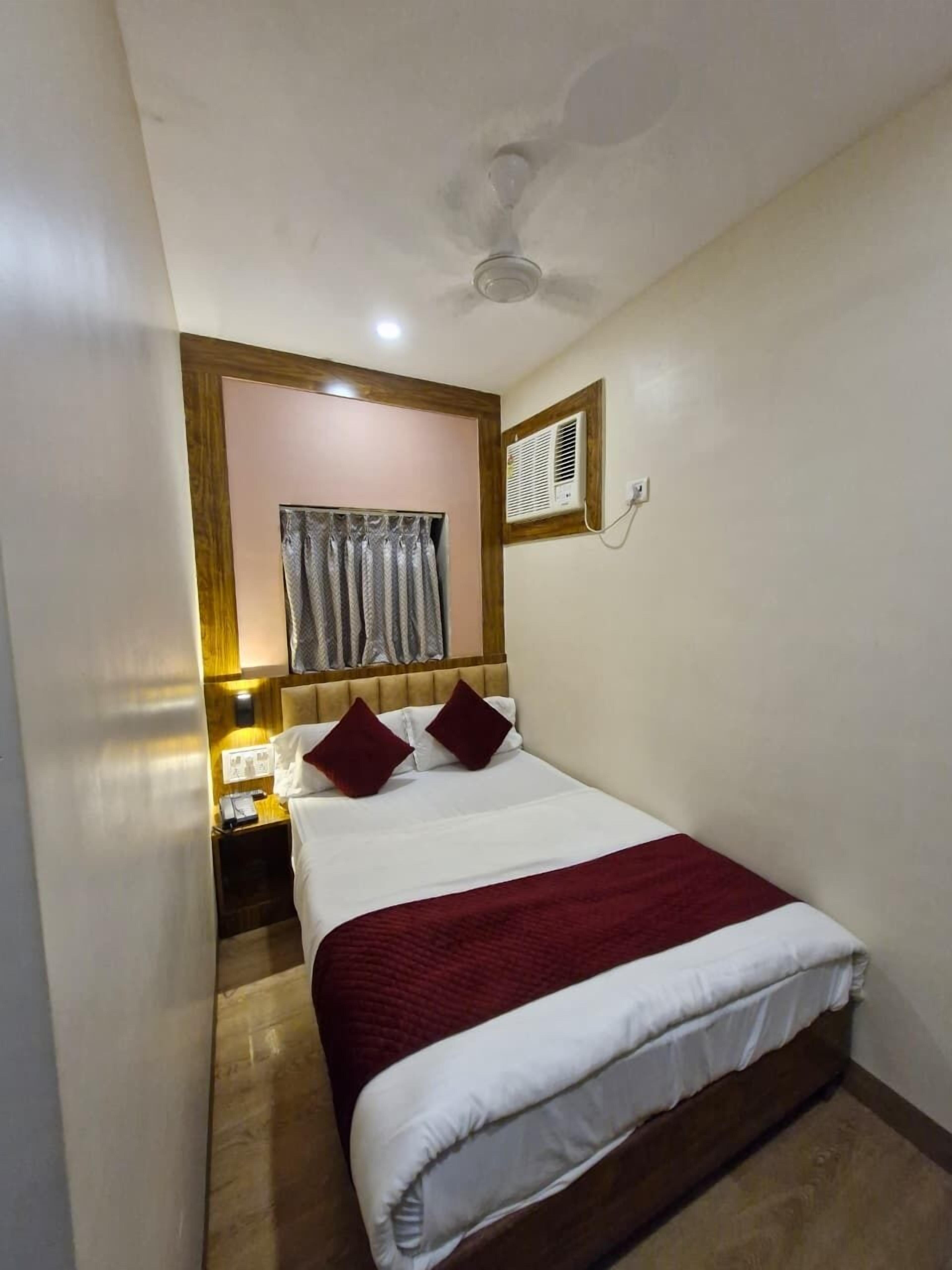 A hotel room with a bed, a nightstand, a wall-mounted air conditioner, and a ceiling fan.