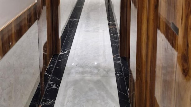 A hallway with wooden doors, a marble floor, and a ceiling fan. - Hotel AL-HAMD (Mumbai)