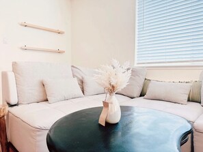 A modern living room with a beige sofa, a round black coffee table, and a vase with dried flowers.