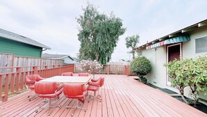 Una terraza de madera con una mesa y sillas, rodeada por una valla de madera y un árbol.