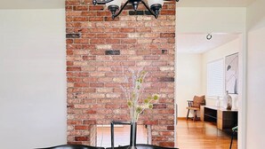 Un comedor con una pared de ladrillo decorativa, una lámpara de araña moderna y un jarrón con flores sobre una mesa de madera.