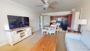 Ein Wohnzimmer mit Fernseher, Couch und Couchtisch. Im Hintergrund ist eine Küchenzeile erkennbar.