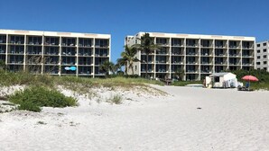 Ein Hotel direkt am Strand mit mehreren Balkonen, einer Strandbar und einer kleinen Konstruktion mit einem roten Sonnenschirm.