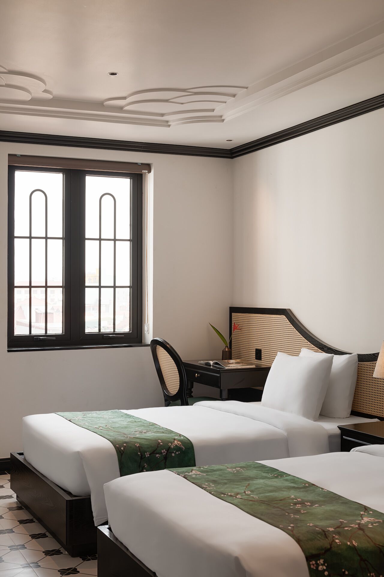 A hotel room with two beds, a desk, a chair, and a large window.