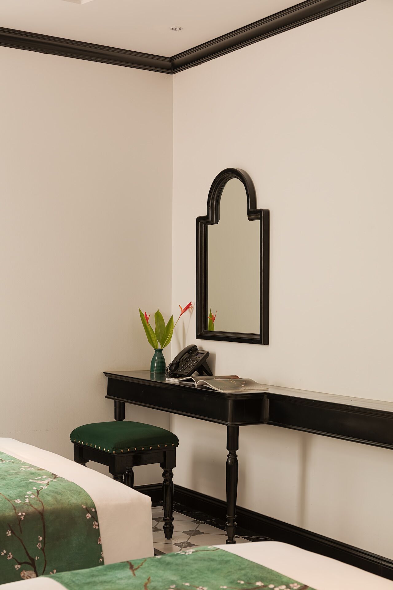 Un dormitorio pequeño y ordenado con una cama individual, una mesita de noche con teléfono y un florero, y un espejo colgado en la pared.