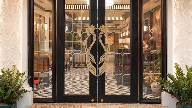La entrada del HOTEL C'IAU, con techo de tejas, puertas dobles con paneles de vidrio decorativo y piso de baldosas a cuadros en el interior.