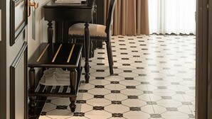 Habitación de hotel con comedor que incluye una mesa negra, una silla y una planta pequeña. La habitación tiene suelo de baldosas y un ventanal con cortinas.