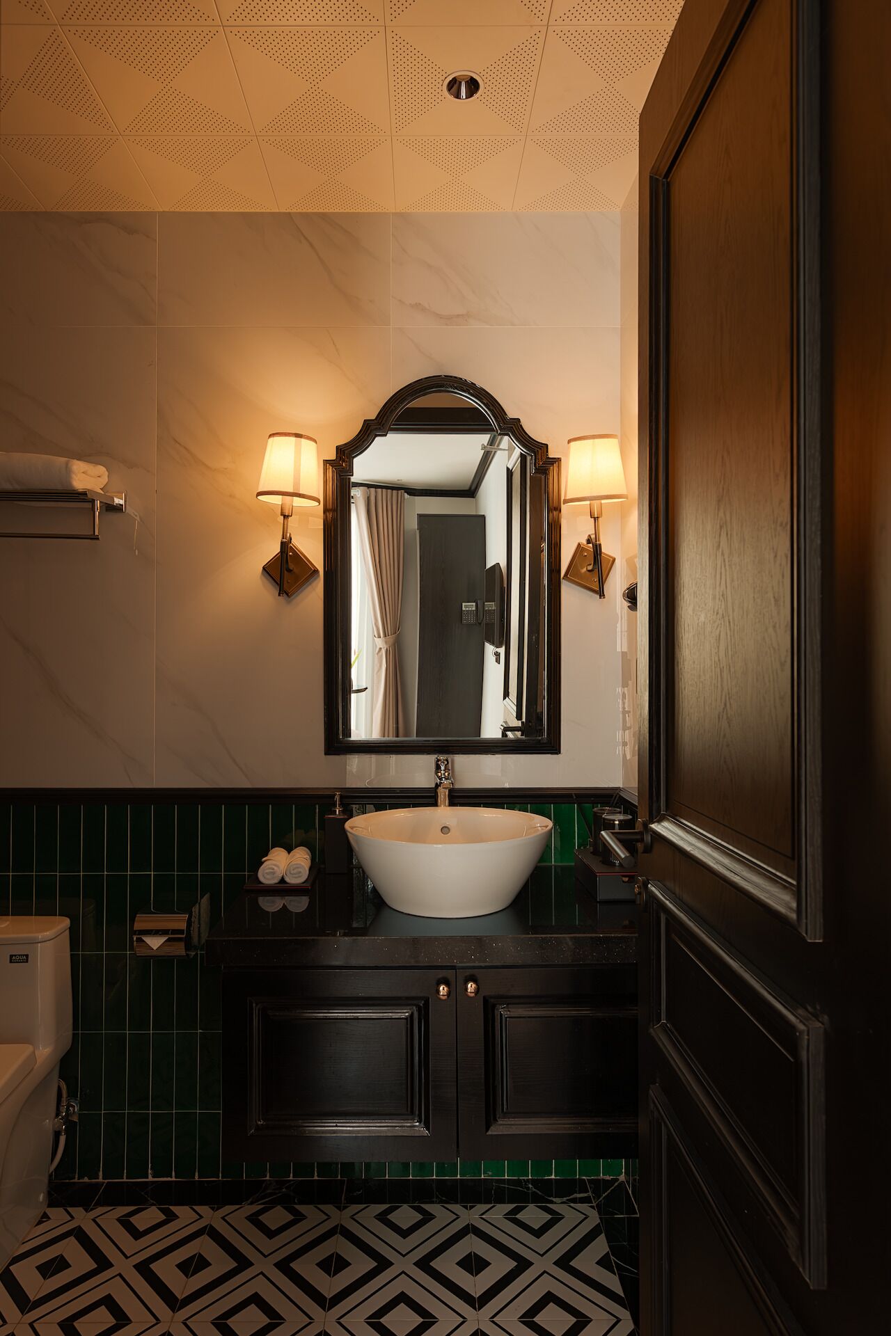 A bathroom with a white sink, dark wood cabinets, green tiled walls, and a mirror with two wall-mounted lamps.