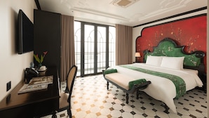 Habitación de hotel con una cama grande, un escritorio con silla, un televisor montado en la pared y una ventana con cortinas.