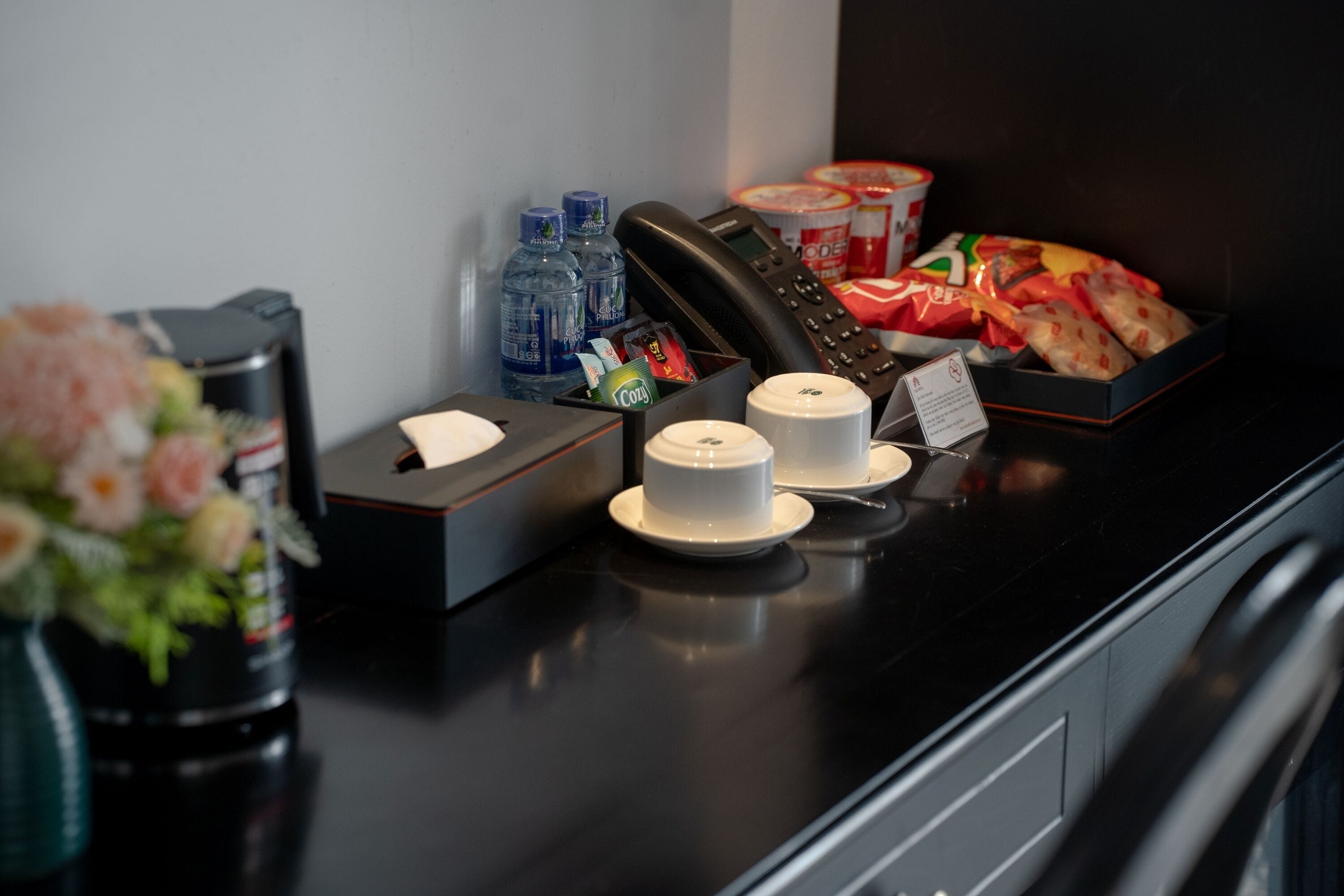 A hotel reception desk with a telephone, bottled water, snacks, and a vase of flowers.