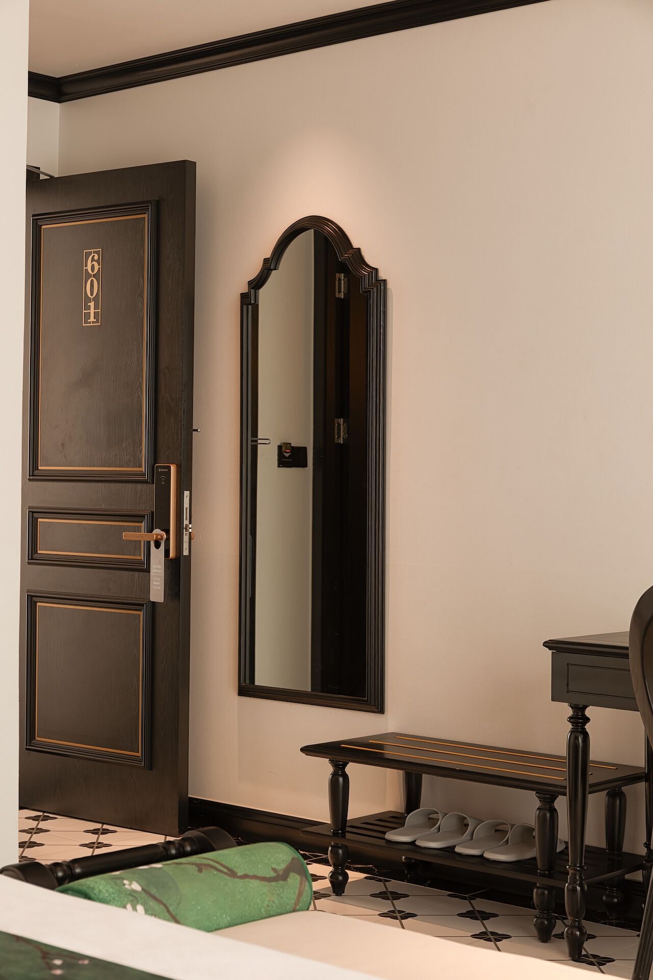 Une pièce avec une porte en bois sombre, un grand miroir, une petite table avec un banc et un porte-chaussures.