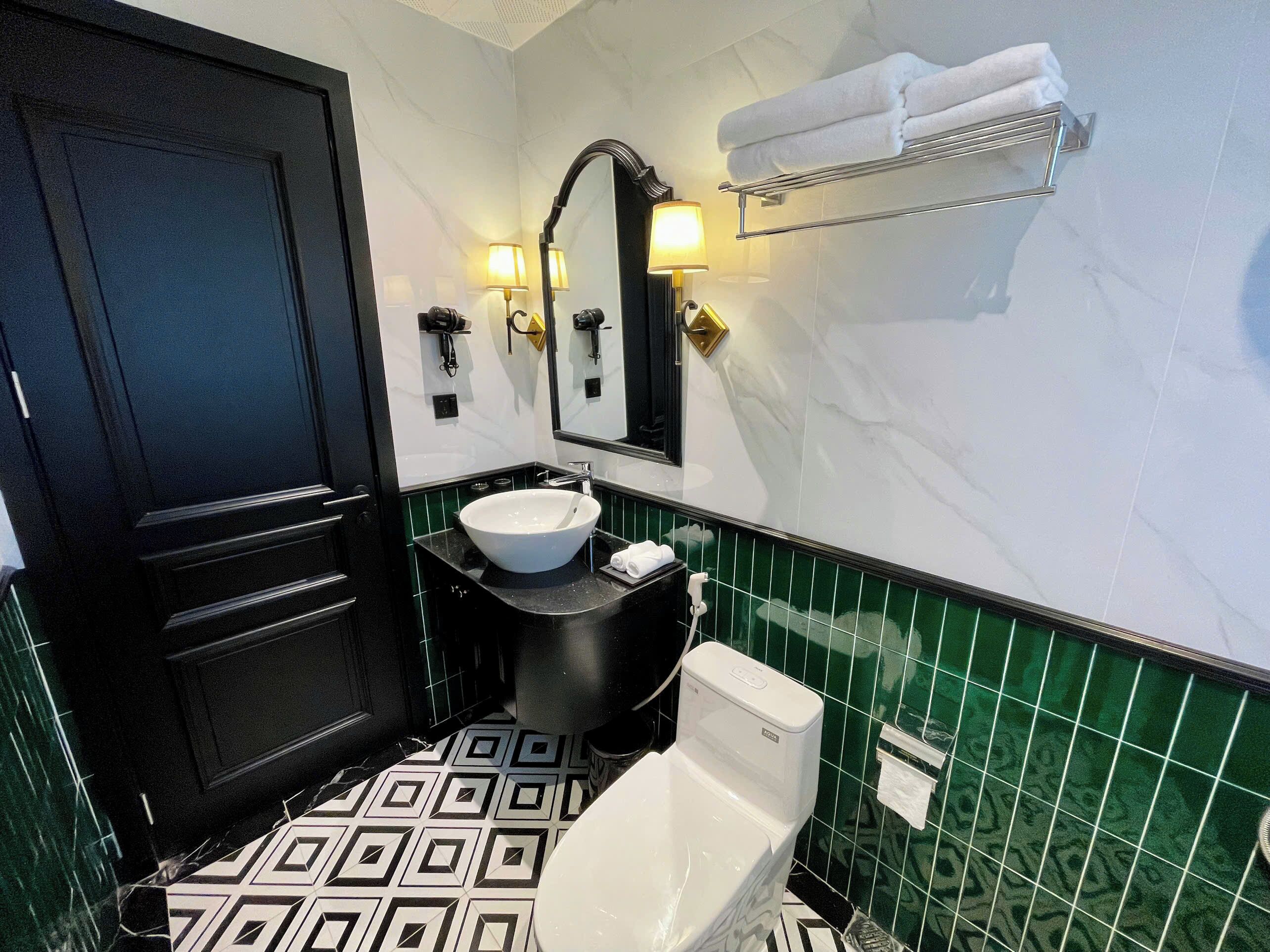 A bathroom with a black door, a white sink, a toilet, and green-tiled walls.