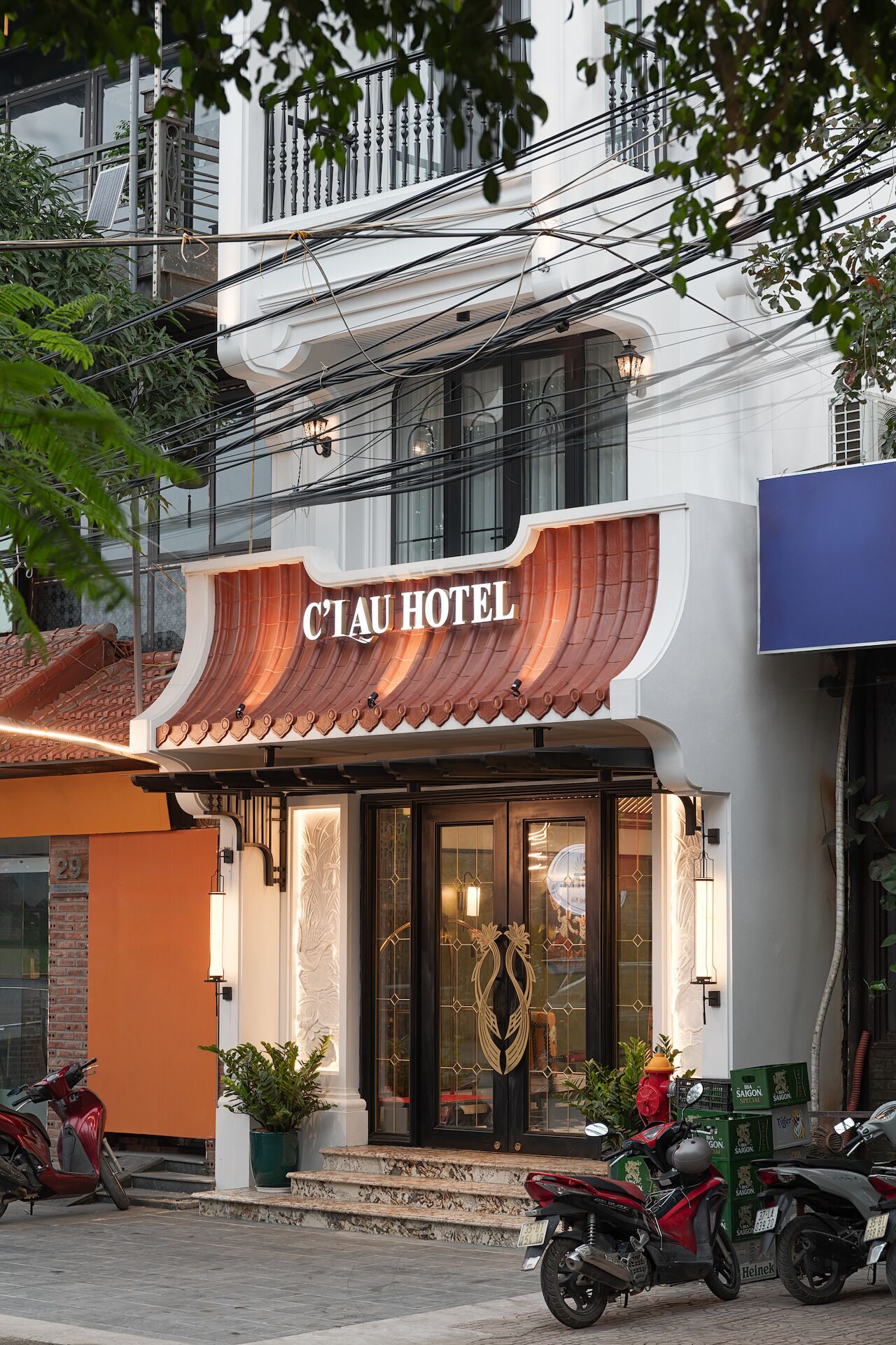 A hotel entrance with a traditional design, a visible address number, and parked motorcycles outside.