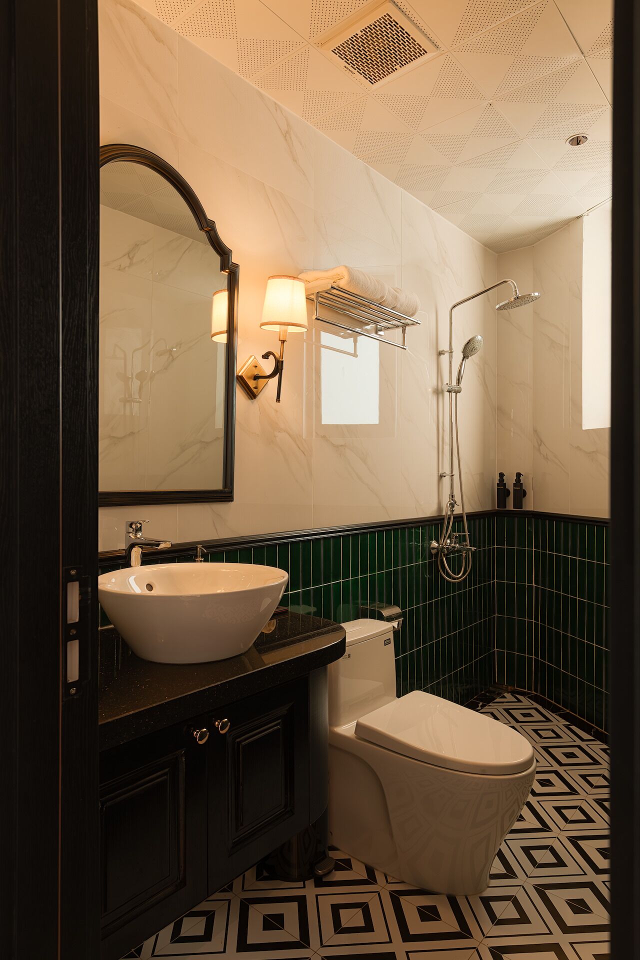 A bathroom with a white sink, dark vanity, a toilet, a shower with a handheld showerhead, and green tiled walls.