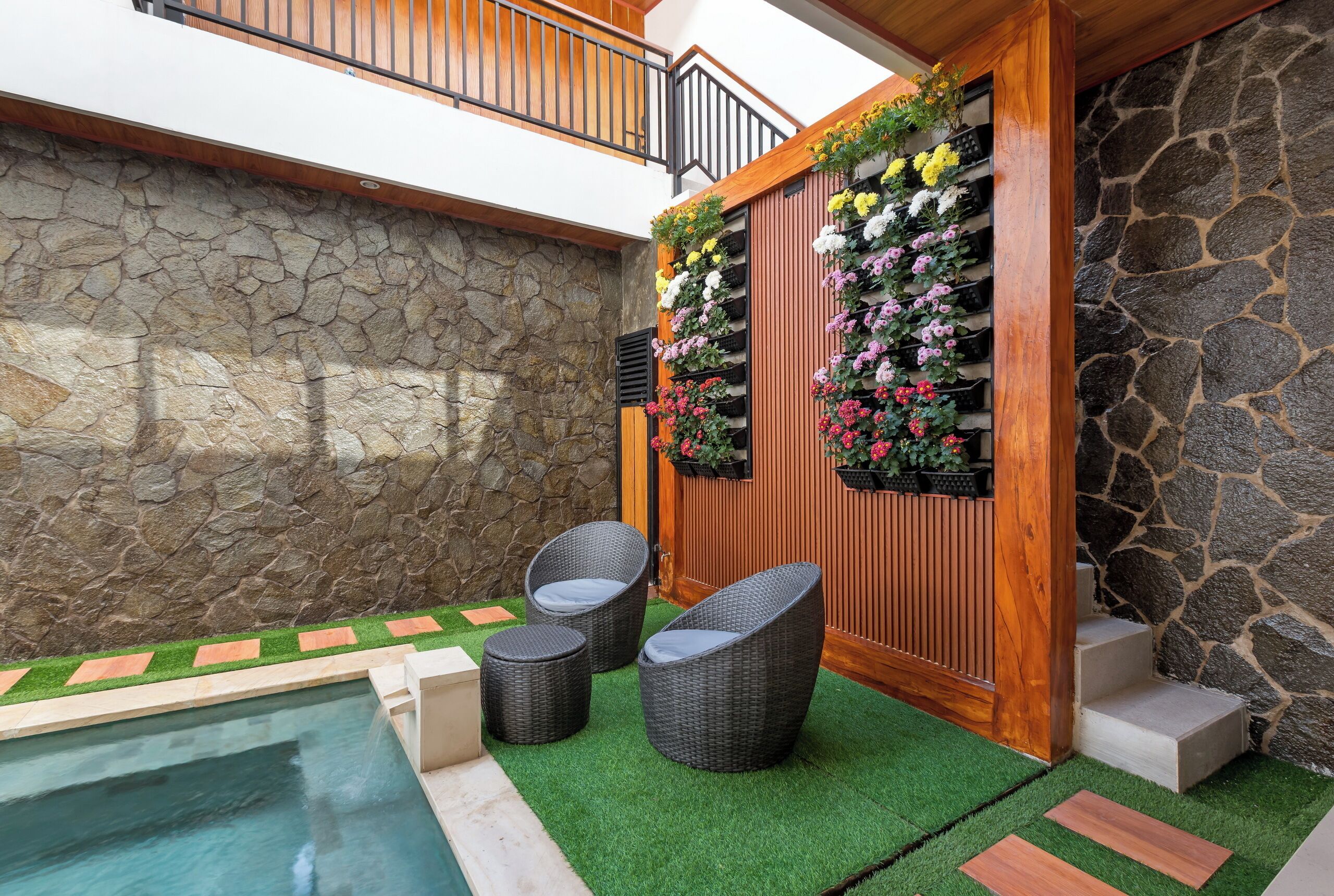 A patio area with a stone wall, a wooden fence with flower planters, a small pool, and wicker chairs.