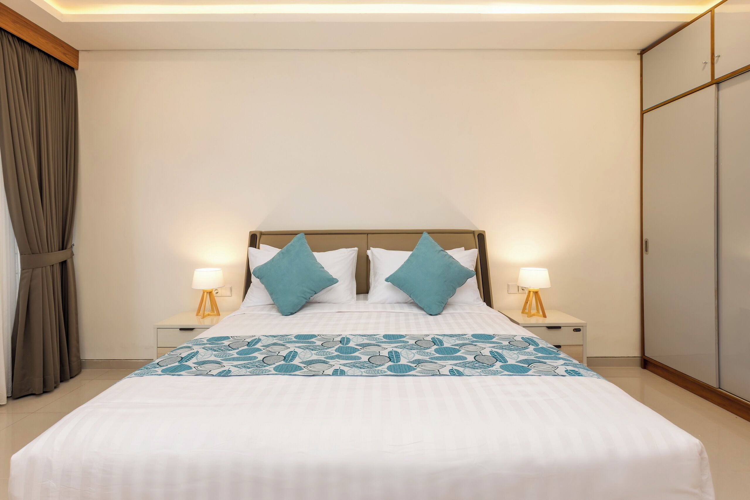 A neatly made bed with a patterned bedspread, two bedside lamps, and a nightstand.