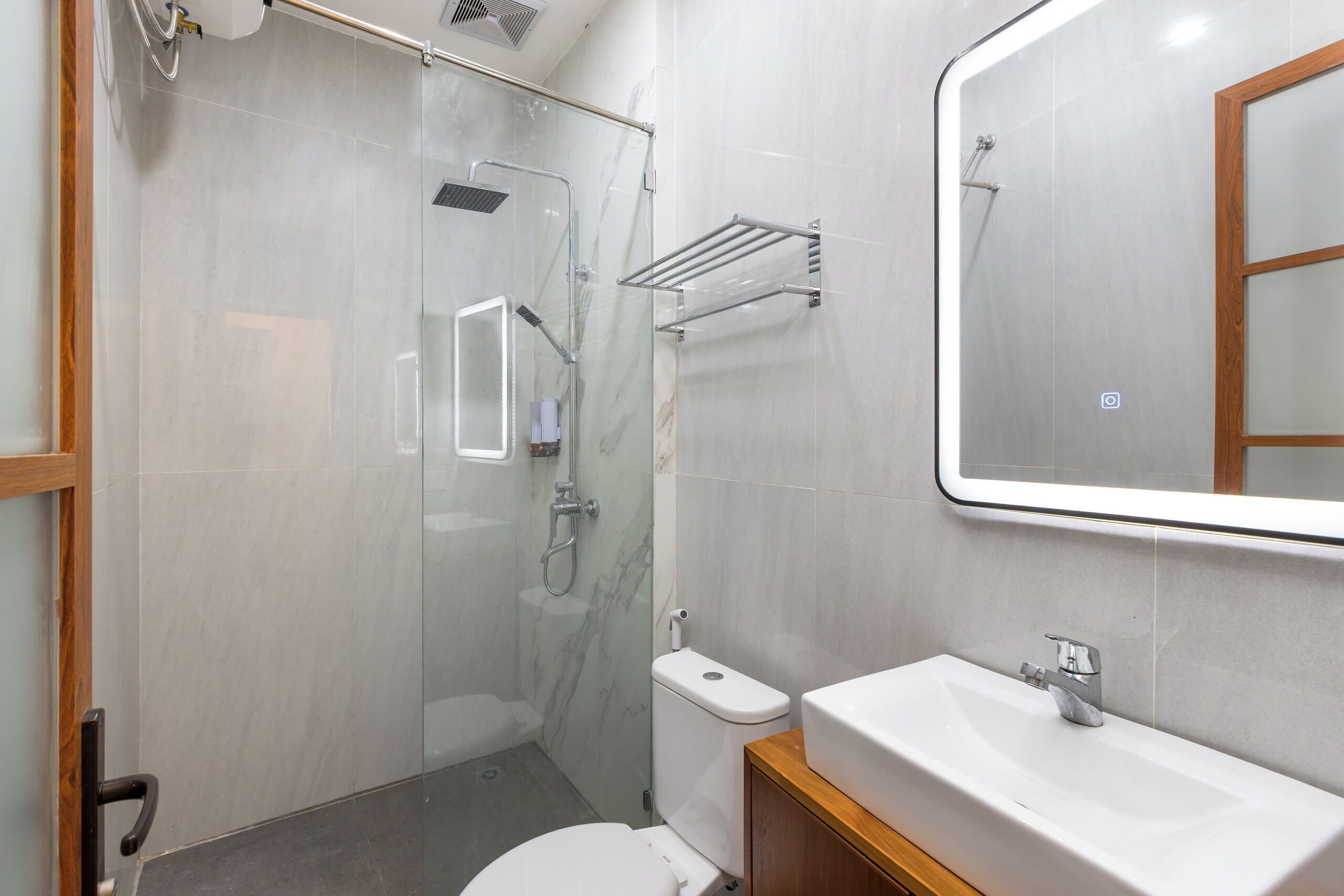 Une salle de bain moderne avec une douche à parois de verre, des toilettes blanches et un lavabo avec un meuble en bois.