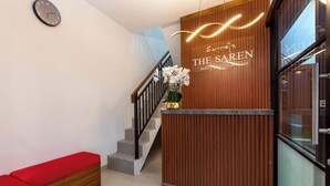 Un comptoir d’accueil avec un panneau décoratif en bois, un escalier avec une rampe noire et un banc rouge.