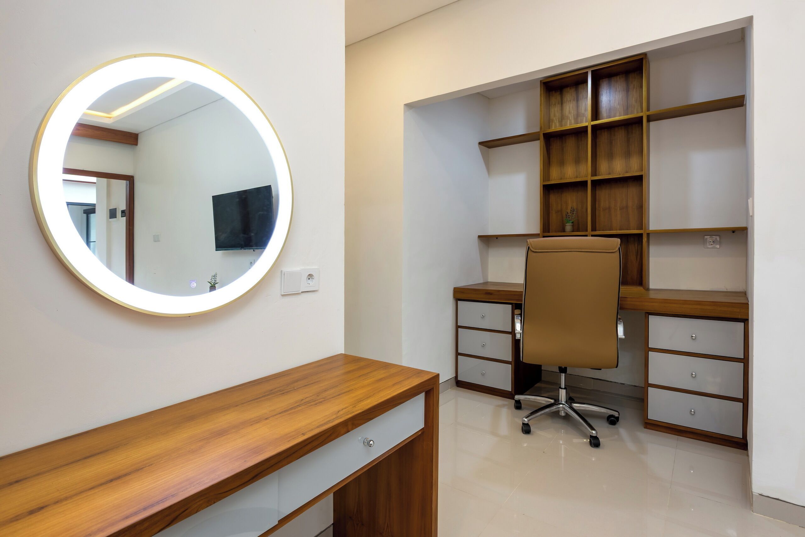 Un espacio de oficina moderno con un escritorio de madera, un espejo redondo, una silla y estanterías empotradas.