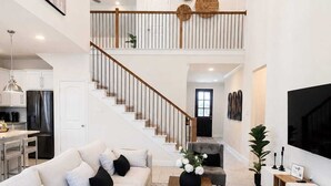 A spacious living area with a large sofa, a coffee table, and a TV. There is a staircase leading to an upper level.