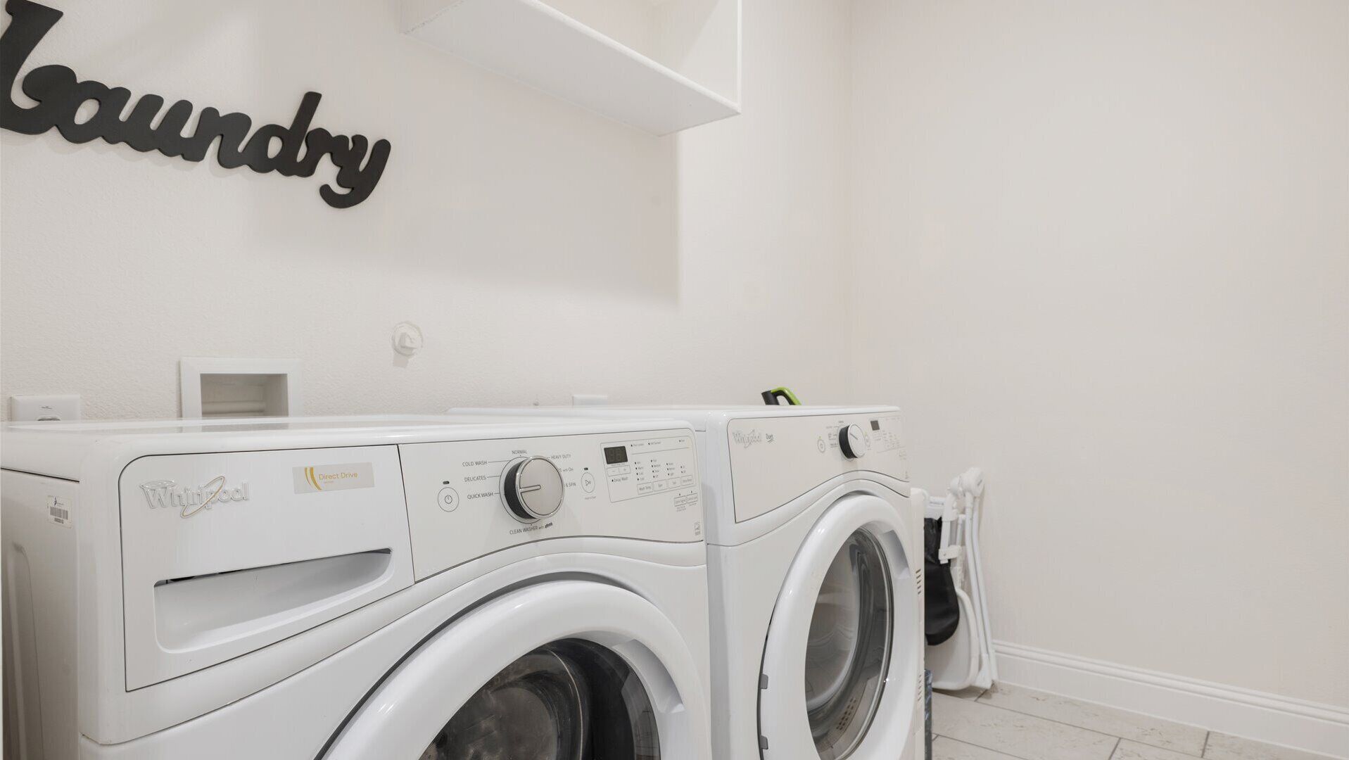 A laundry area with two front-loading washers and dryers, a white wall, and a 'Laundry' sign.
