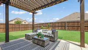 An outdoor patio with wicker furniture, a glass-top coffee table, and a pergola overhead.