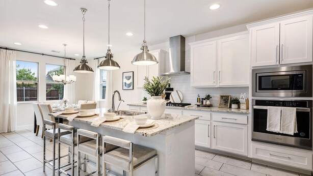 A modern kitchen with white cabinetry, stainless steel appliances, and pendant lighting.