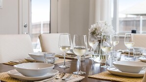 A dining table set with white plates, bowls, and wine glasses, with a vase of white flowers in the center.