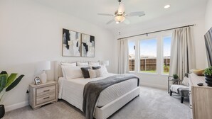 A bedroom with a bed, bedside tables, a ceiling fan, artwork, a window with curtains, and a view of the outside.
