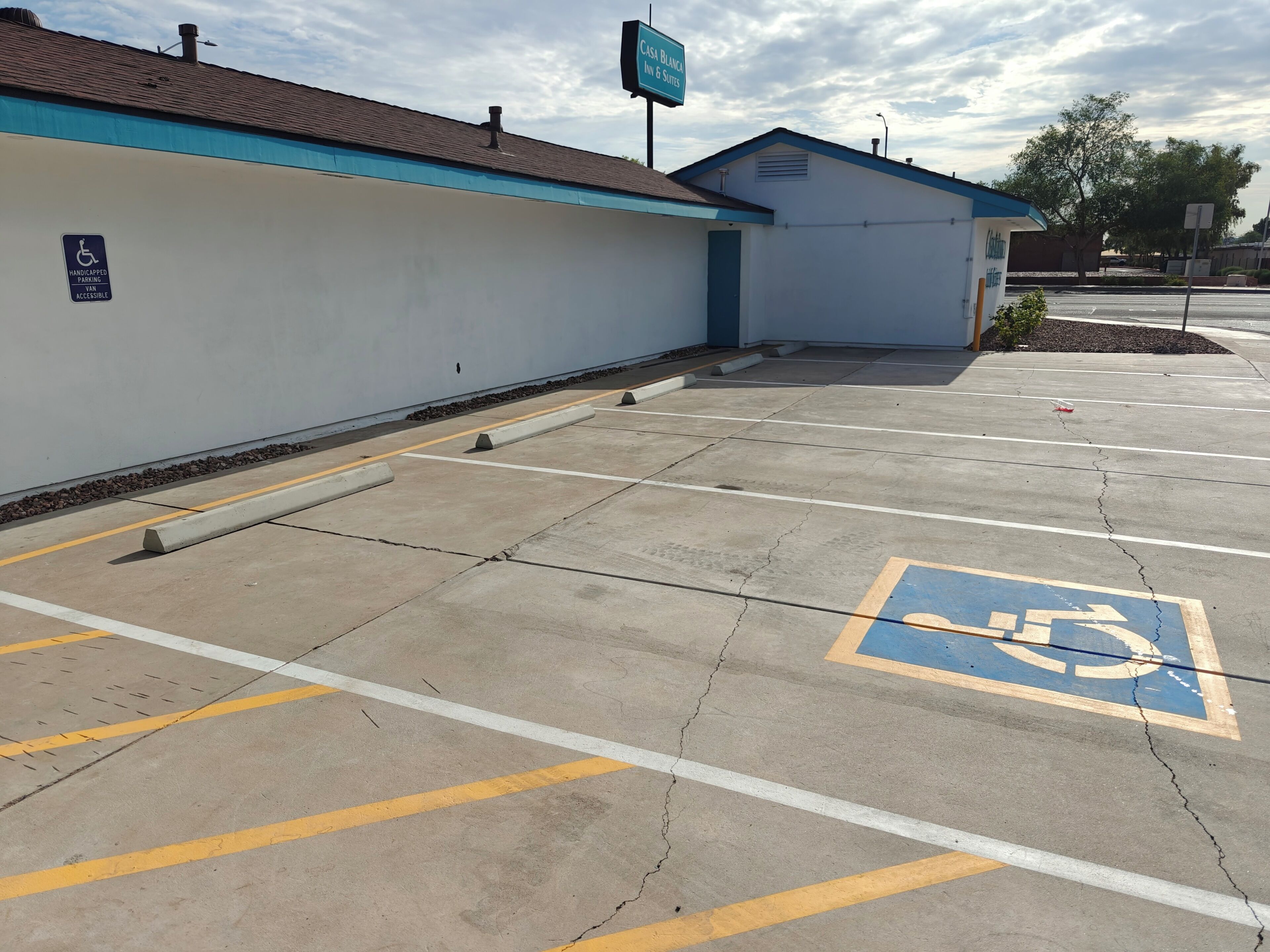 Un parking avec des places réservées aux personnes handicapées, un bâtiment avec un toit bleu et une enseigne indiquant « Casa Blanca Inn & Suites ».