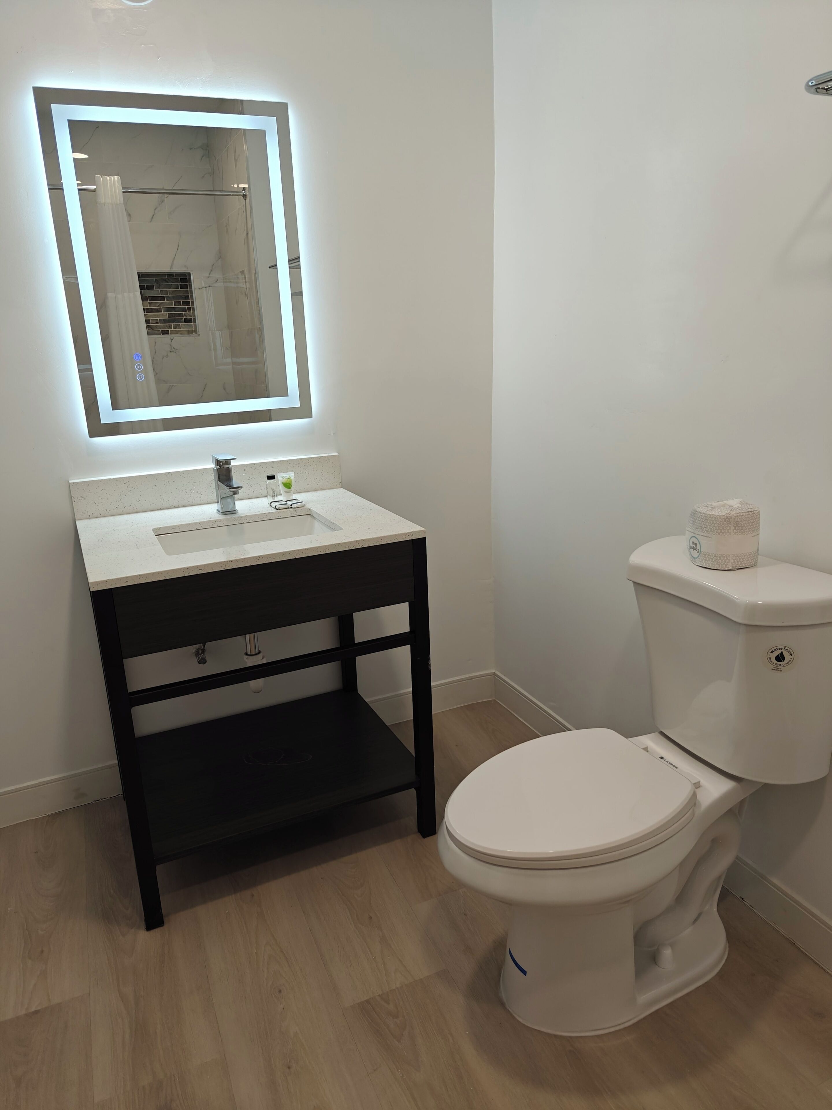 Un baño con inodoro blanco, lavamanos con espejo y tocador de madera oscura.