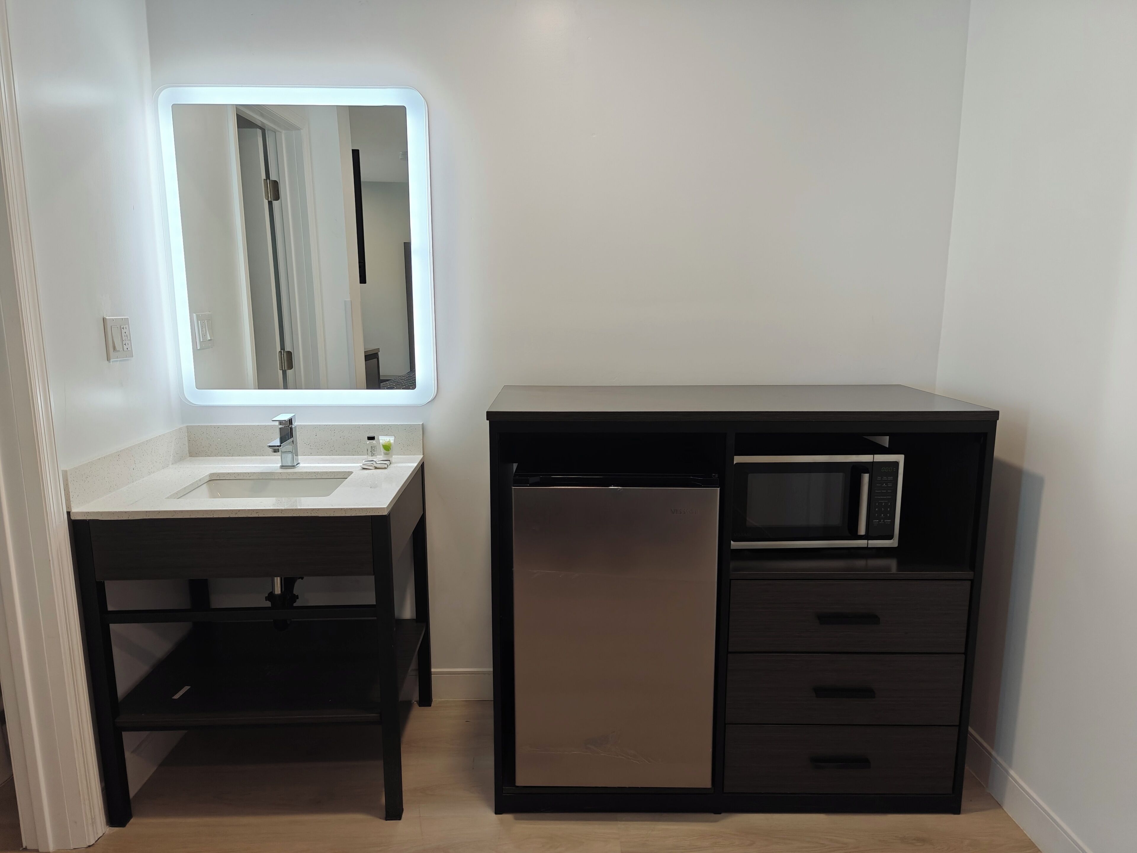 Un baño pequeño con lavamanos, espejo y microondas integrado.