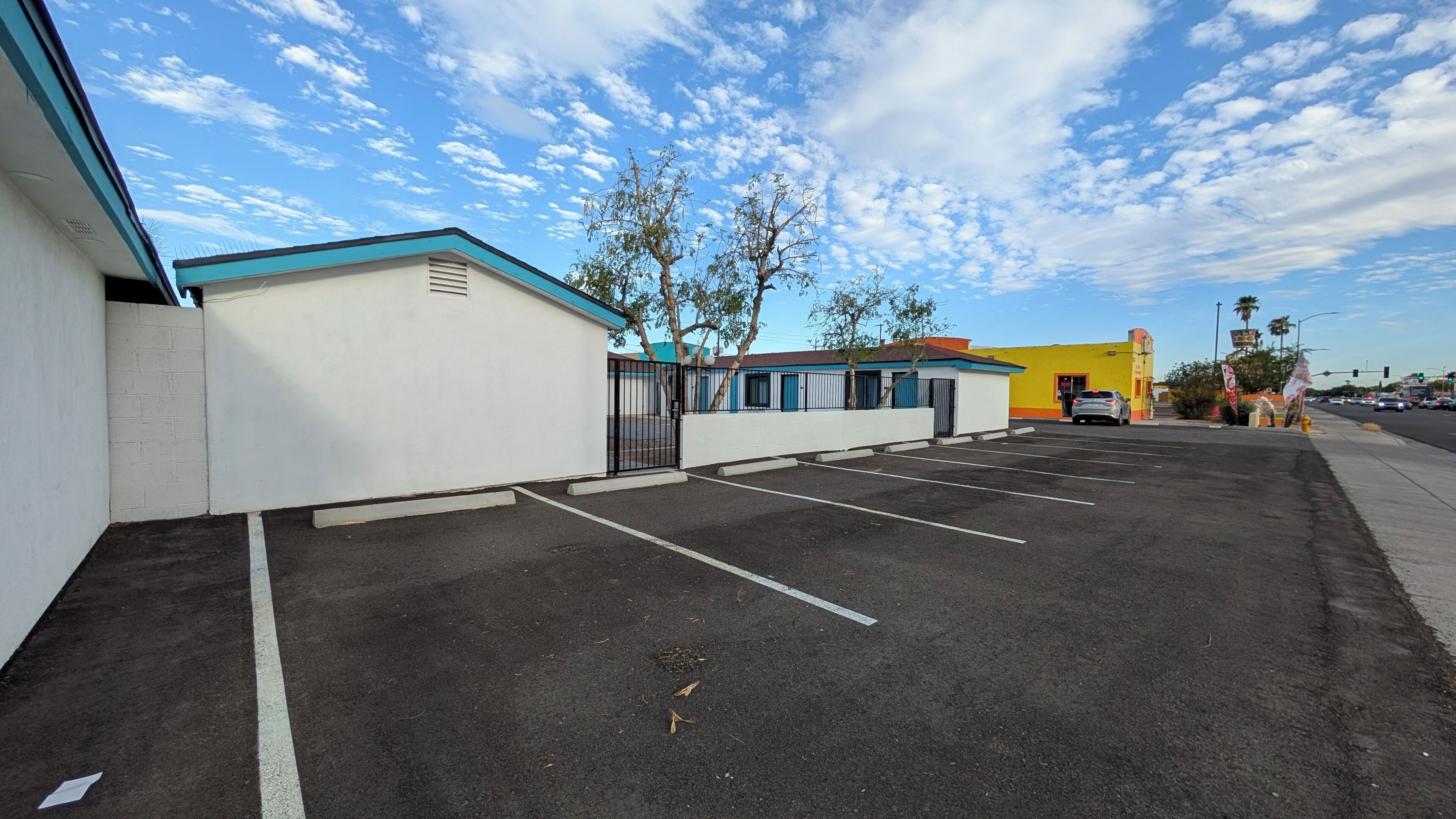 A parking lot with marked spaces, a gated entrance, and a building with a blue roof.
