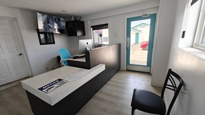 A reception area with a desk, a blue chair, a computer, and a TV mounted on the wall. - Casa Blanca Inn and Suites (Chandler)
