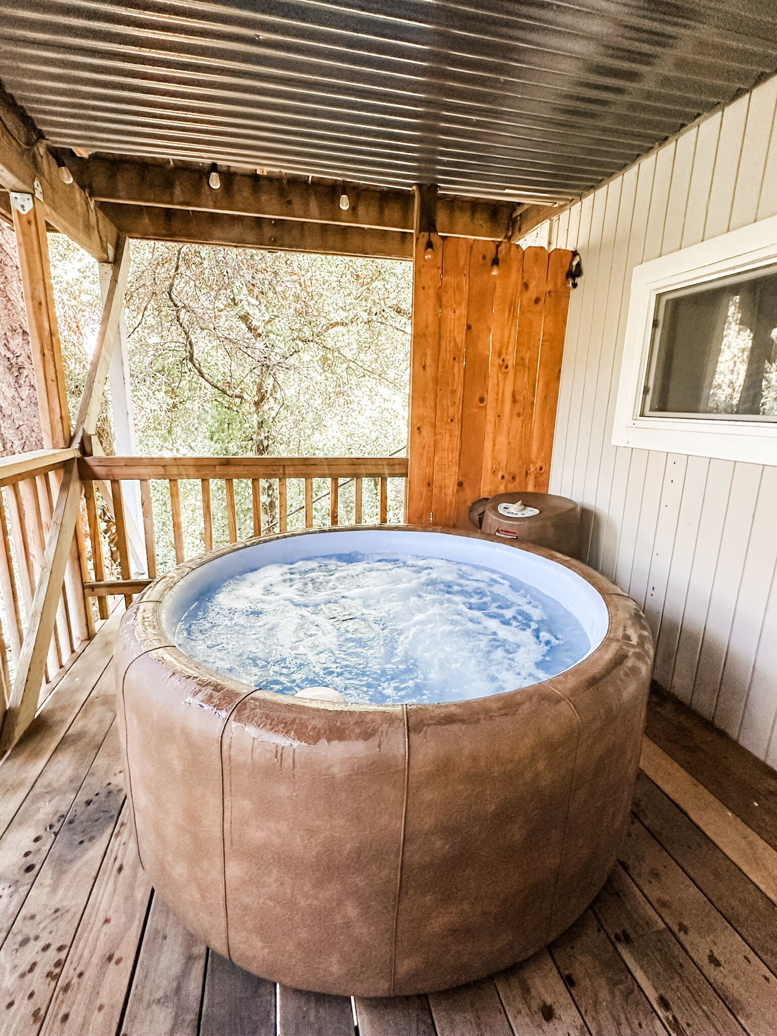 A hot tub on a wooden deck with a metal roof and a window.