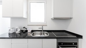 Une cuisine moderne avec des meubles blancs, un plan de travail noir, un évier en acier inoxydable, un grille-pain, une bouilloire et une machine à café.