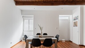 Un coin repas comprenant une table en bois, quatre chaises, un vase avec des plantes et une fenêtre avec des stores.