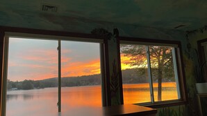 A room with a large window overlooking a lake at sunset.