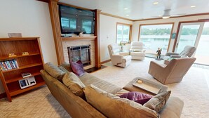 A living room with a fireplace, a television, a sofa, and a view of a lake.