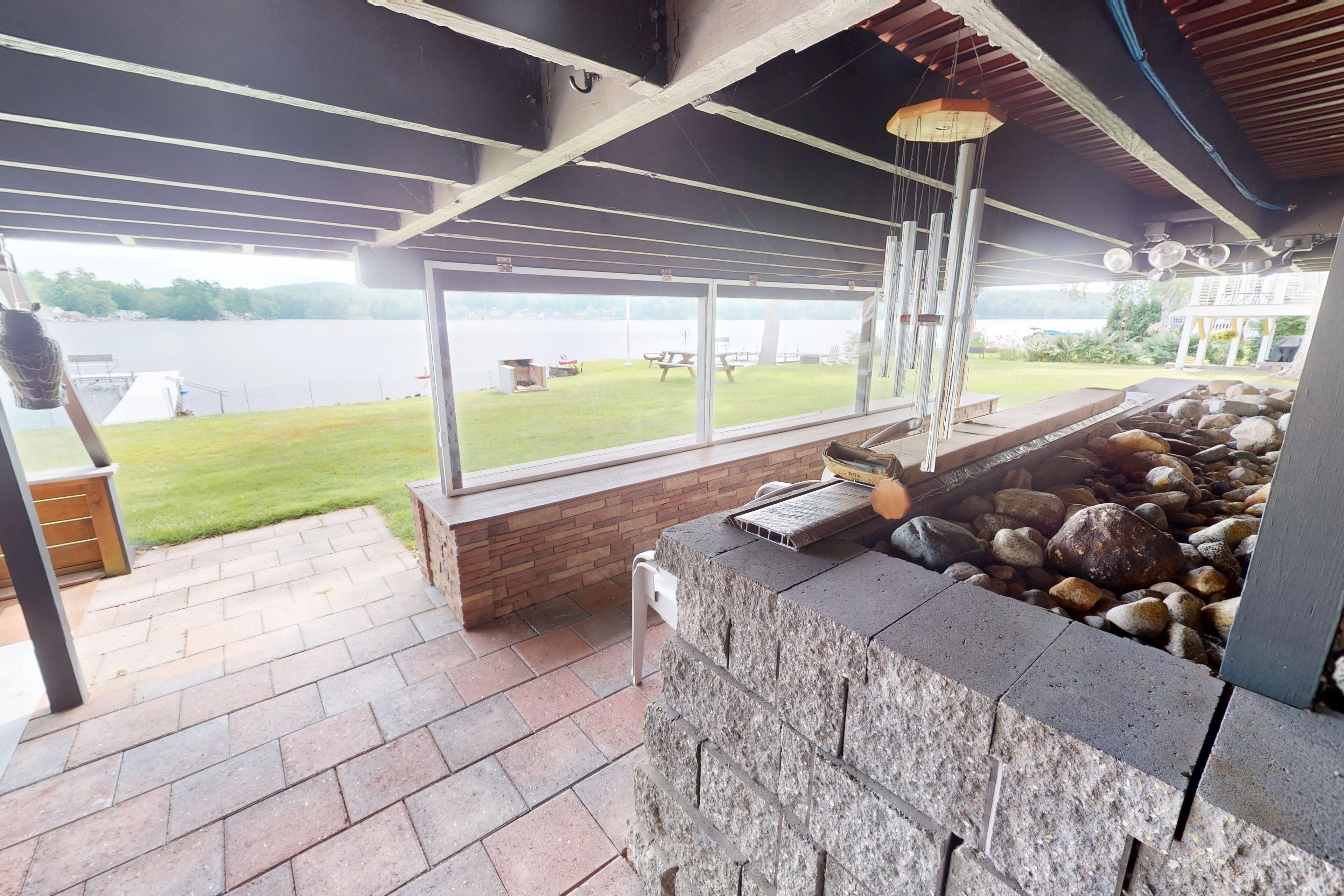 Un'area patio coperta con un muro in pietra, un barbecue e vista su un lago.