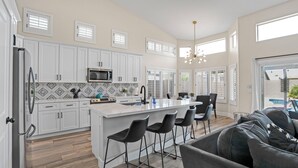 A modern kitchen with white cabinets, a central island with bar stools, a microwave, and a chandelier. - Spacious 4 BR -SaltwaterHotTub -Pool -Sleeps 11 (Peoria)