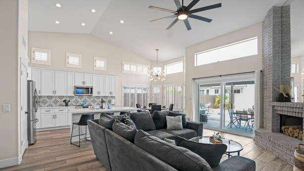 A spacious living room with a gray sectional sofa, a dining area with a table and chairs, a kitchen with white cabinets and a microwave, and a fireplace. - Spacious 4 BR -SaltwaterHotTub -Pool -Sleeps 11 (Peoria)