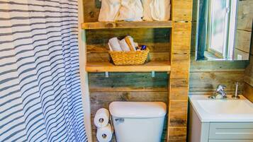 A bathroom with a striped shower curtain, wooden shelves with towels and toiletries, a white toilet, and a sink.