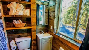 Un baño rústico con paredes de madera, un inodoro blanco, un lavabo y estantes con toallas y artículos de aseo.