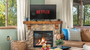 A living room with a stone fireplace, a television displaying 'NETFLIX', a couch, and a coffee table with snacks.