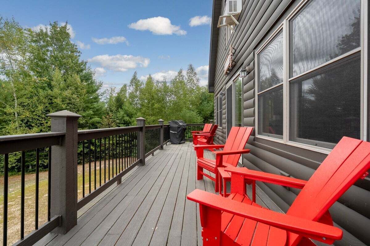 A wooden deck with red chairs, a black railing, and a view of trees.